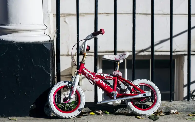 Kleine rode kinderfiets met witte banden geparkeerd tegen een zwart hek