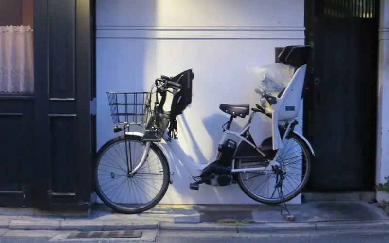 Twee fietsen met kinderzitjes voor en achter tegen een witte muur